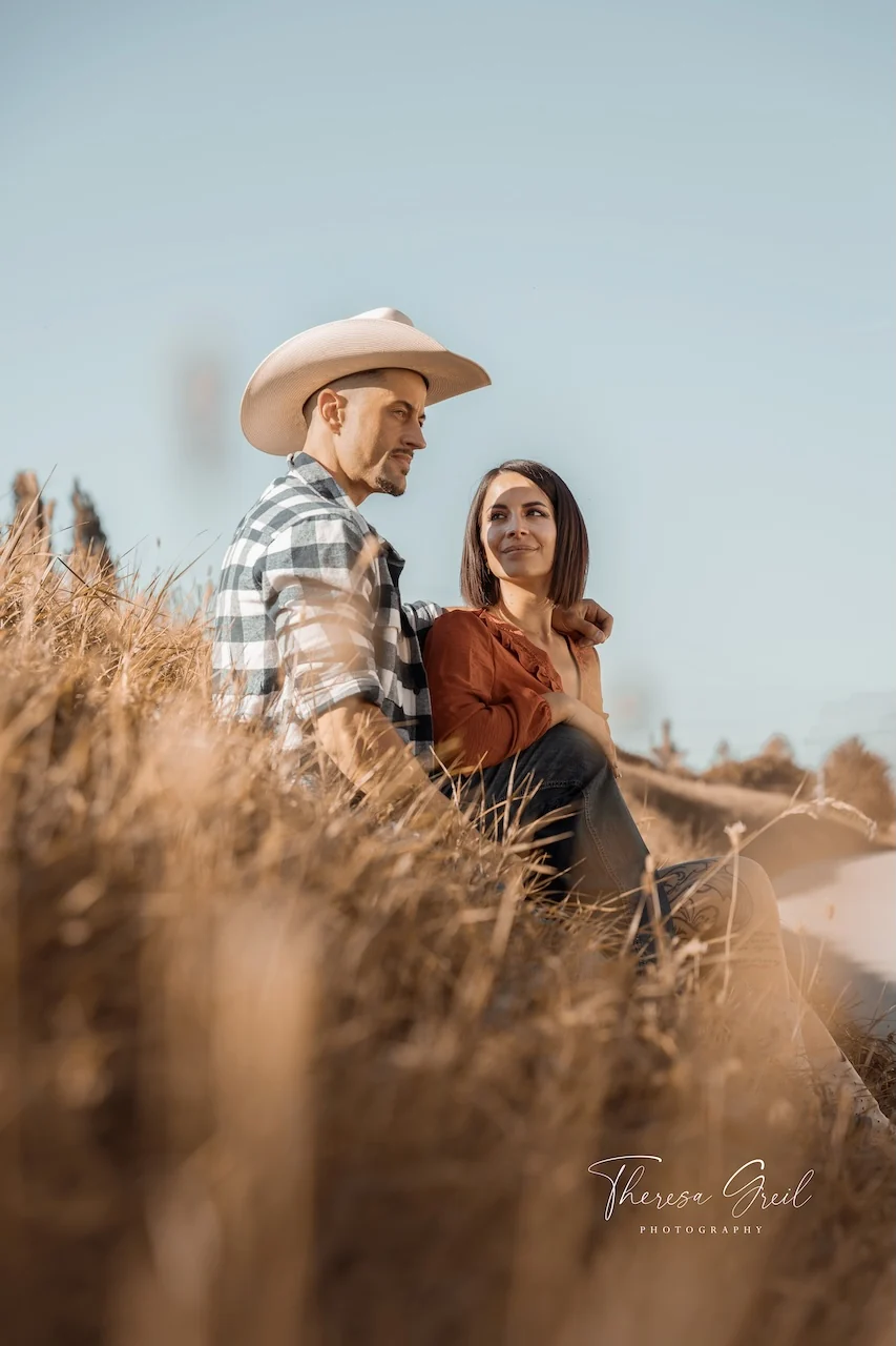 Johann Laurent mit Cowboyhut und Selina Hempel von der Laurent Ranch sitzen gemeinsam im hohen Gras