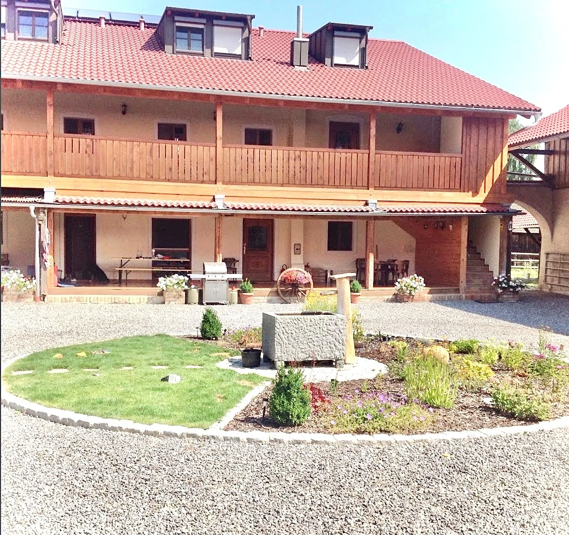 Rundes Zierbeet mit Steintrog vor dem Gebäude mit Holzbalkon auf der Laurent Ranch in Gottfrieding
