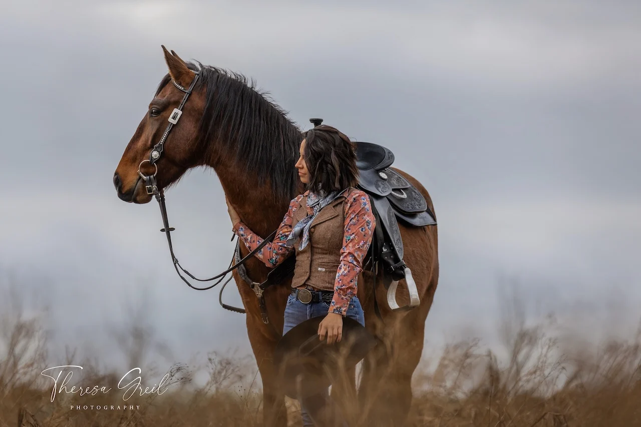 Selina Hempel mit Cowboyhut neben einem braunen Pferd mit Westernsattel auf der Laurent Ranch