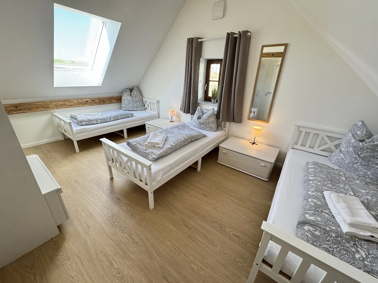 Dreibettzimmer im Apartment der Laurent Ranch in Gottfrieding mit drei weißen Holzbetten unter der Dachschräge, Dachfenster und Spiegel
